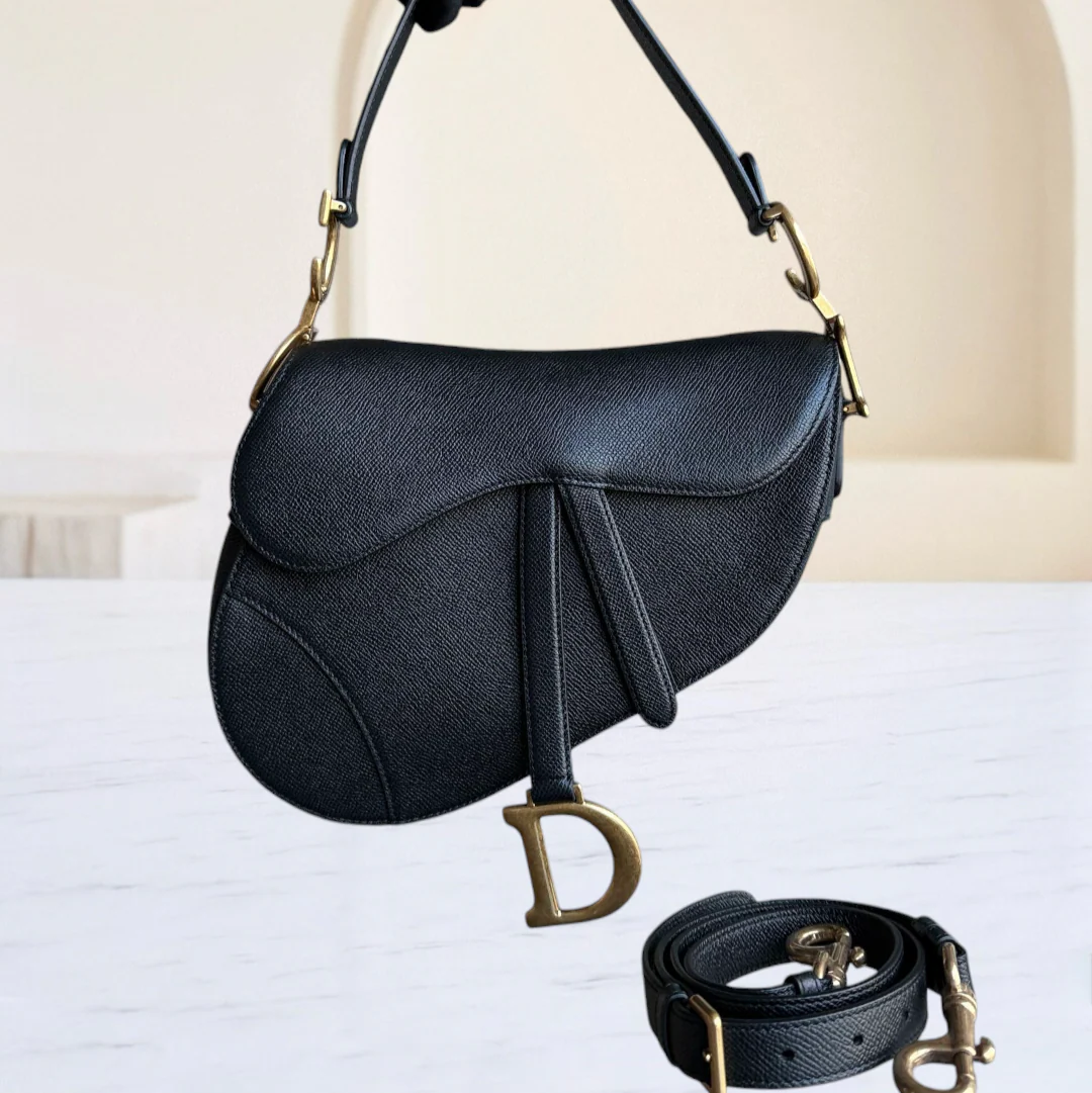 Black handbag with gold accents held by a gloved hand on a light background