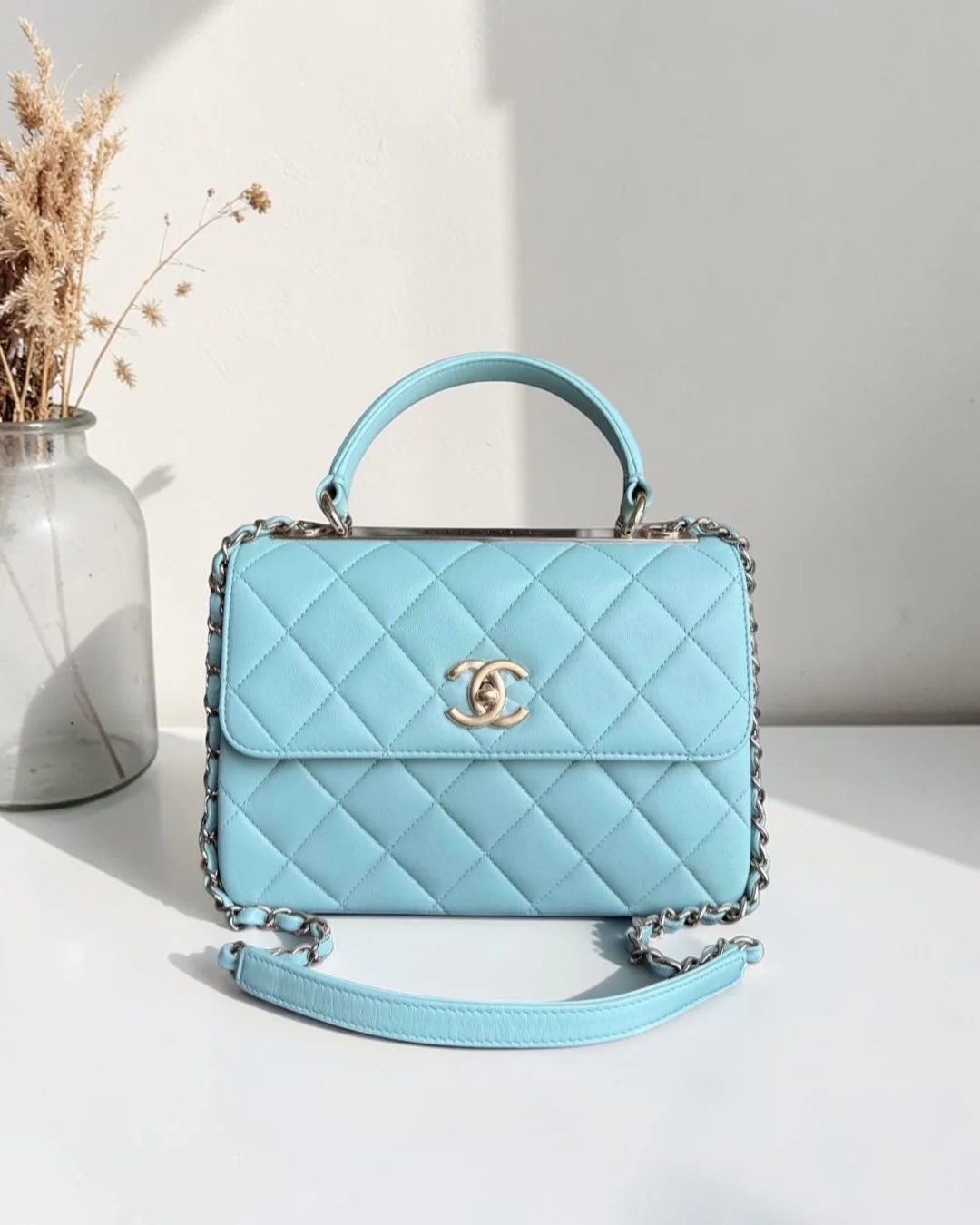 Light blue quilted Chanel handbag on a black mat with a white background