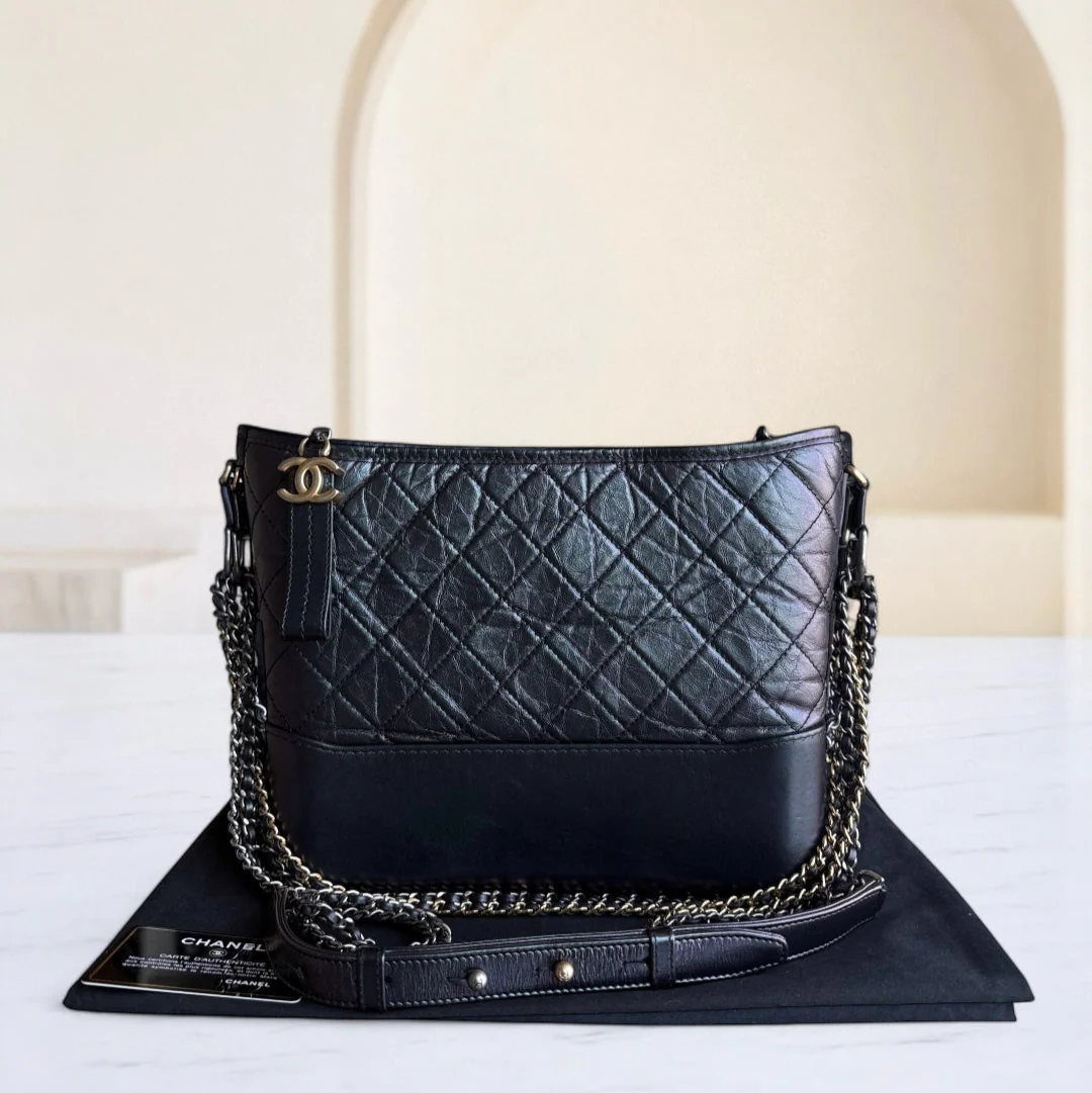 Black quilted handbag with gold chain detail on a white surface