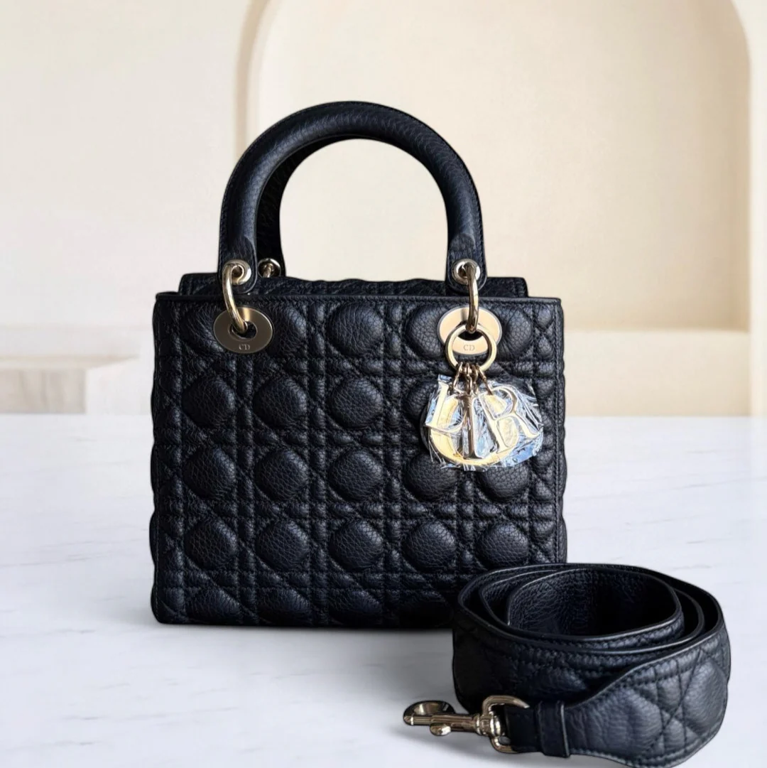 Black quilted handbag with gold hardware and a clear crystal charm on a white surface.