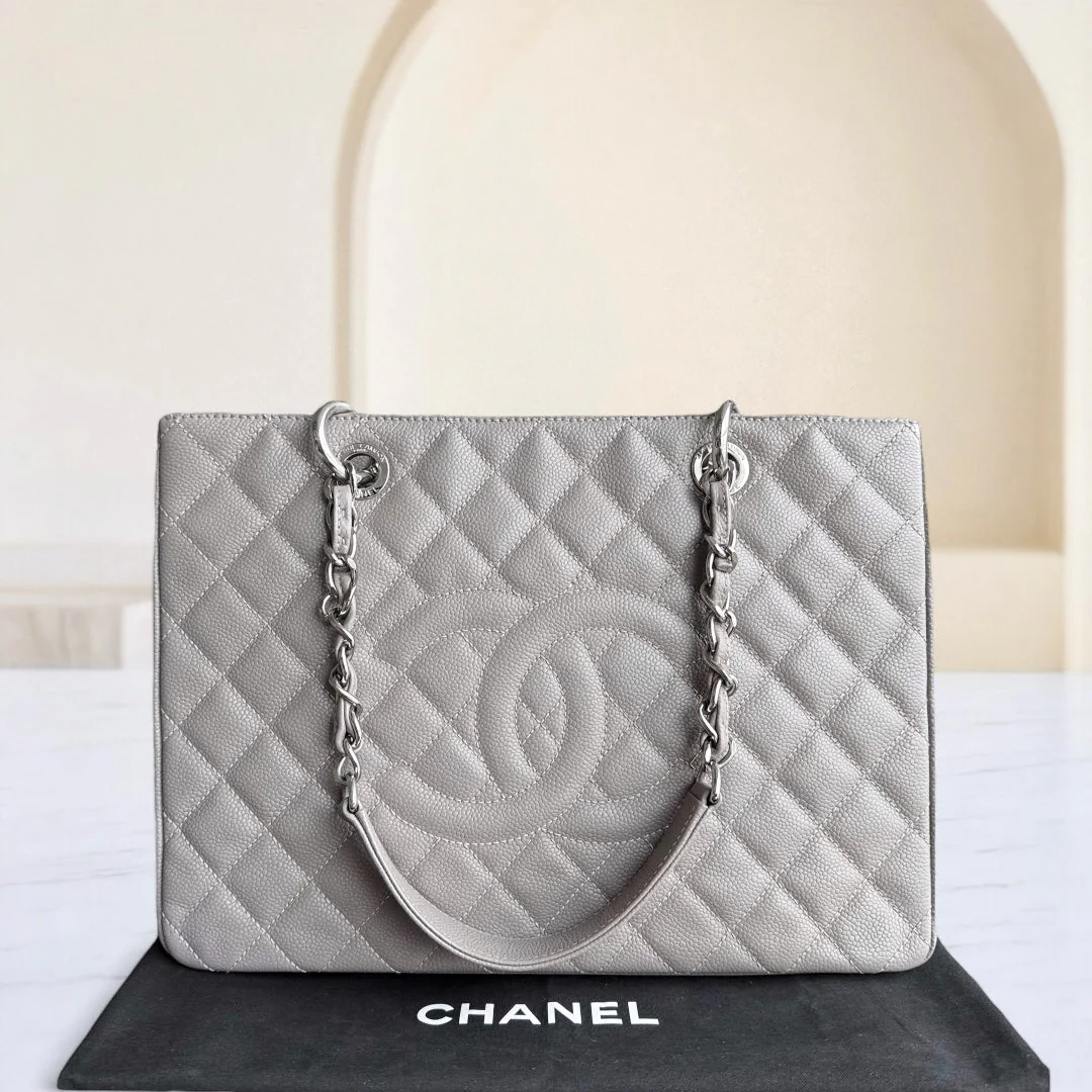 Gray quilted Chanel handbag on a white surface with a beige background