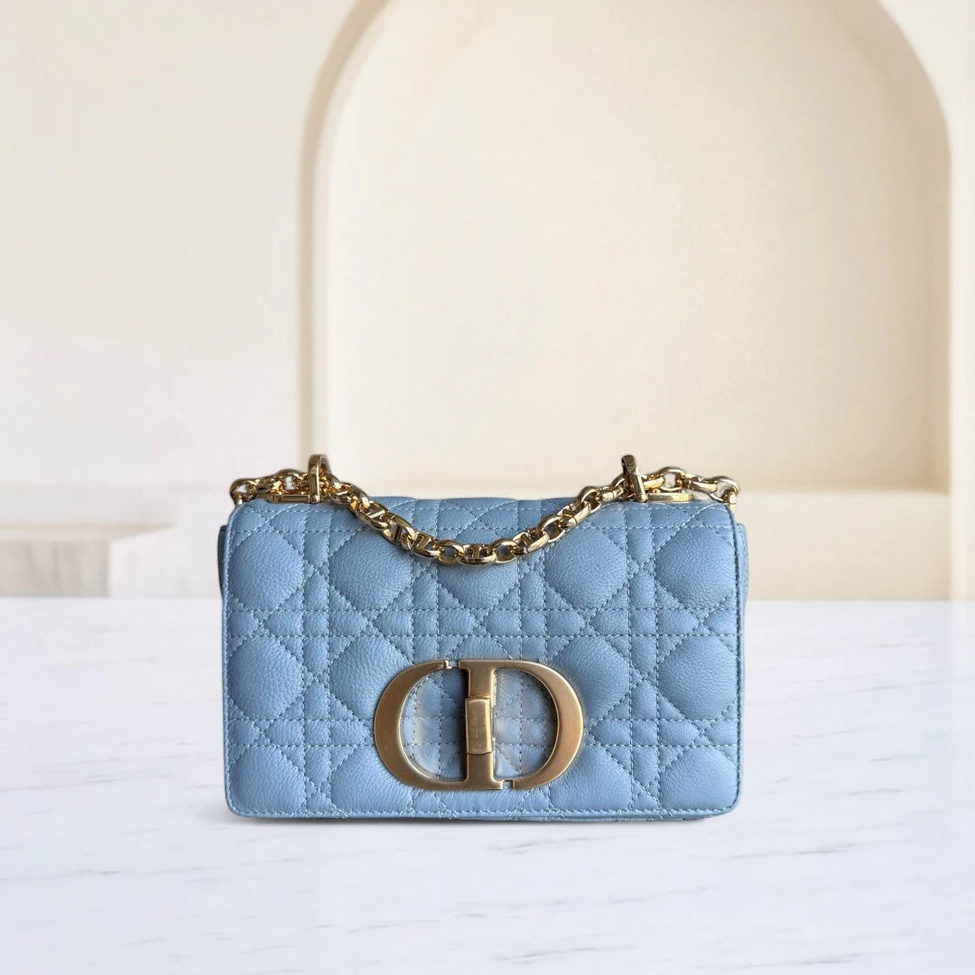 Light blue handbag with gold chain and logo on a white surface