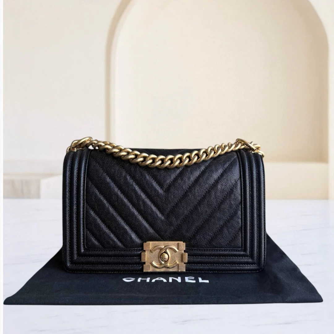 Black Chanel handbag with gold chain and clasp on a white surface.