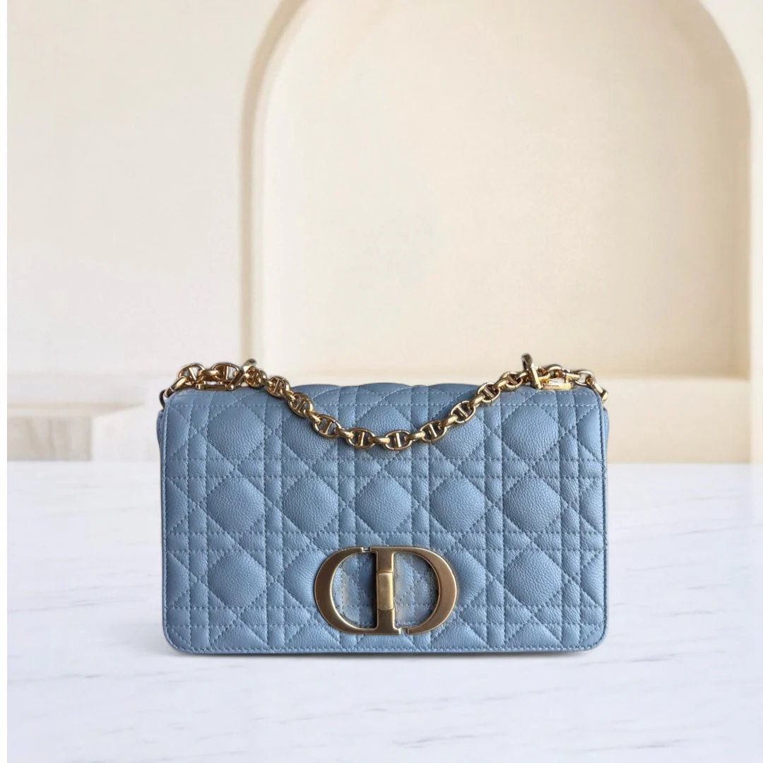 Blue quilted handbag with gold chain and clasp on a white surface