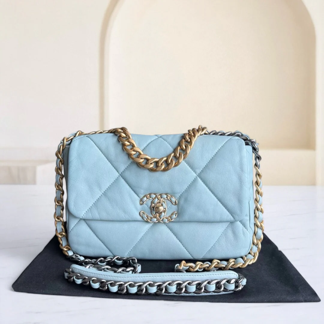 Light blue quilted handbag with gold chain on a black mat against a white background