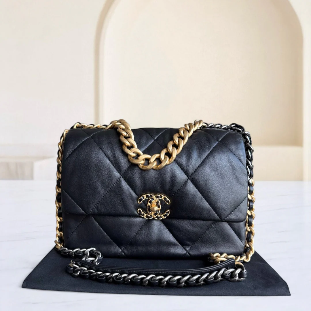 Black quilted handbag with gold chain and logo on a white surface.
