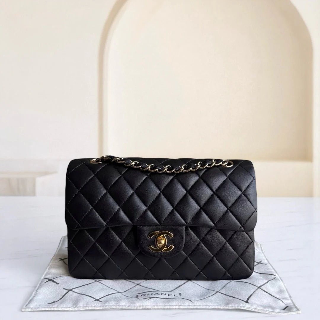 Black quilted handbag with gold chain on a white surface with a blurred background