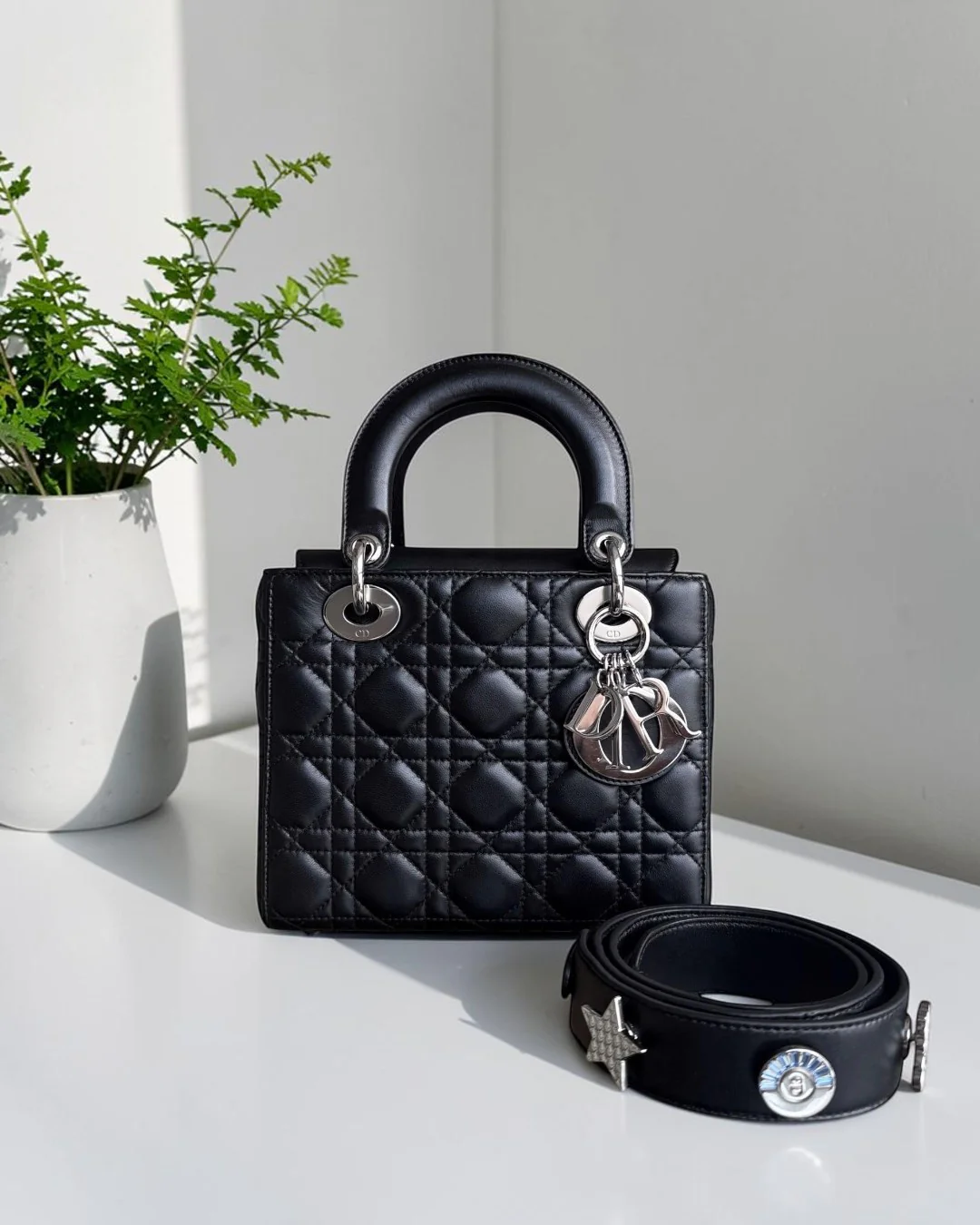 Best Luxury Designers black lambskin Dior Lady Small Flap bag with silver hardware and charms, shown with a decorative strap.